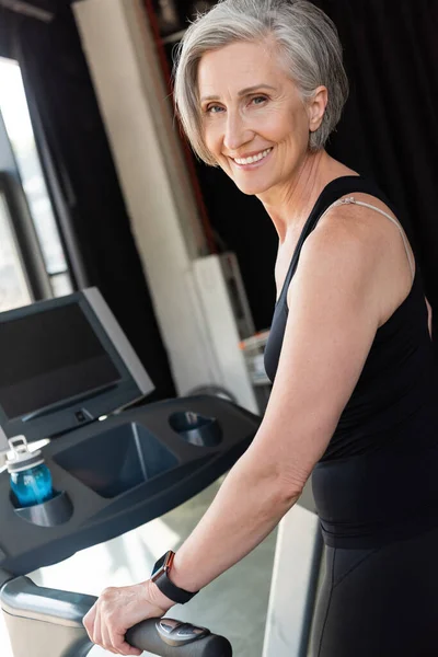 Щаслива старша жінка з сірим волоссям вправляється на біговій доріжці в спортзалі — стокове фото