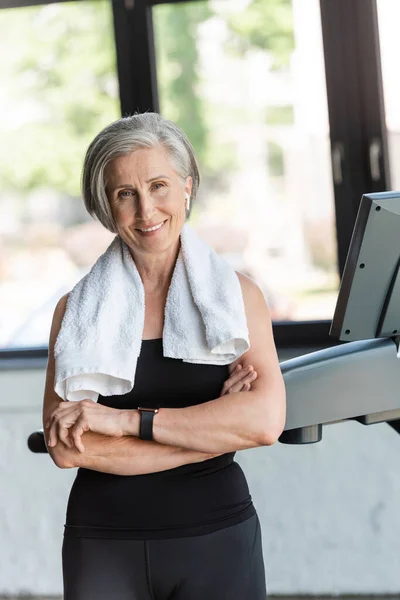 Positive Seniorin mit weißem Handtuch auf den Schultern neben Laufband — Stockfoto
