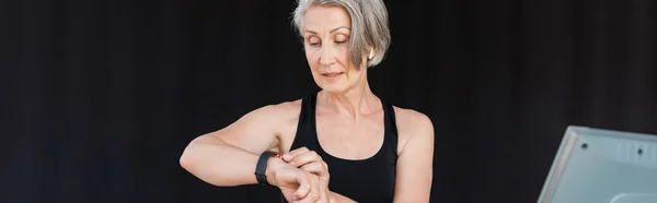 Mujer mayor con actividad de comprobación de pelo gris en el rastreador de fitness en el gimnasio, pancarta - foto de stock