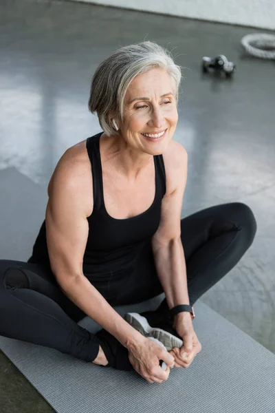 Blick aus der Vogelperspektive auf eine glückliche Seniorin, die auf der Fitnessmatte im Fitnessstudio lächelt — Stockfoto