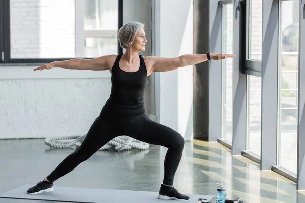 Полная длина спортивной формы пожилая женщина в черной спортивной одежде, тренирующаяся с протянутыми руками в тренажерном зале — стоковое фото