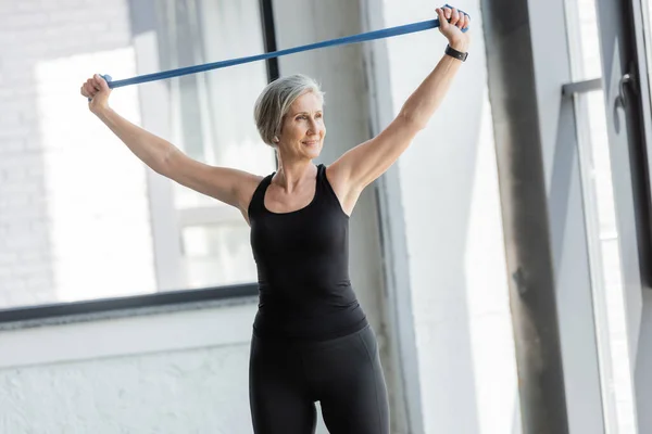 Happy senior woman in black sportswear working out with resistance band above head — Stock Photo