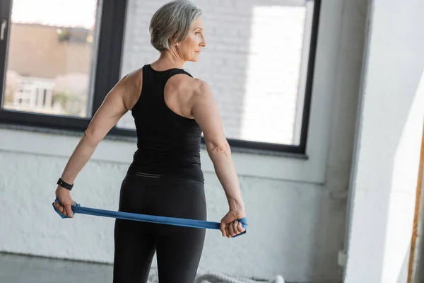 Fit senior woman working out with resistance band in sports center — Stock Photo
