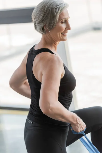 Overjoyed senior woman in black leggings and tank top exercising with elastics — Stock Photo
