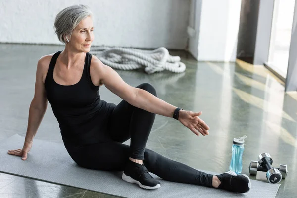 Intera lunghezza della donna anziana in leggings neri e allenamento canotta sul tappeto fitness in palestra — Foto stock