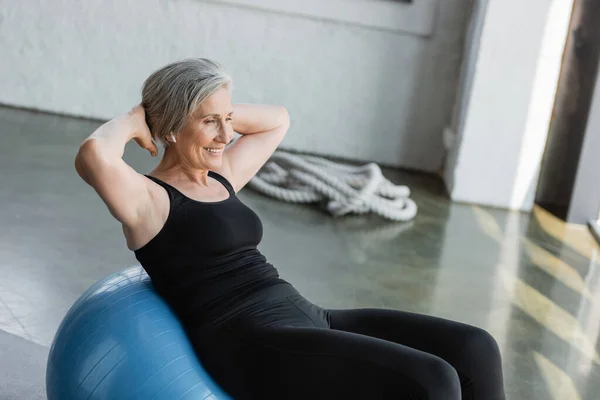 Cheerful senior woman in black leggings and tank top exercising on fitness ball — Stock Photo