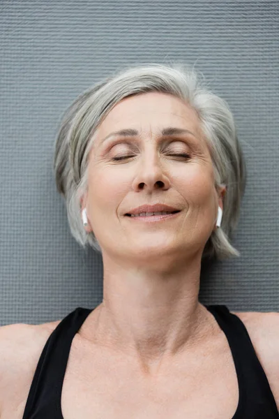 Top view of happy senior woman in wireless earphones lying on fitness mat — Stock Photo