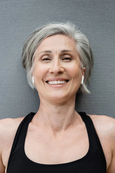 Vista superior da mulher sênior alegre em fones de ouvido sem fio deitado no tapete de fitness — Fotografia de Stock