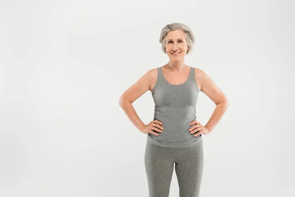 Happy senior woman in tank top standing with hands on hips isolated on grey — Stock Photo