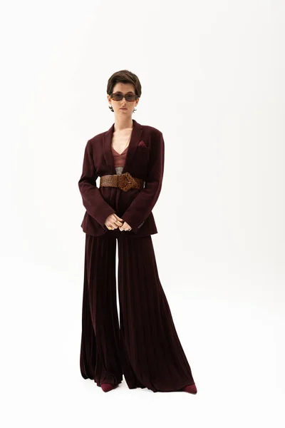 Longitud completa de la mujer elegante en pantalones de palazzo y chaqueta marrón con cinturón de cuero sobre fondo blanco - foto de stock