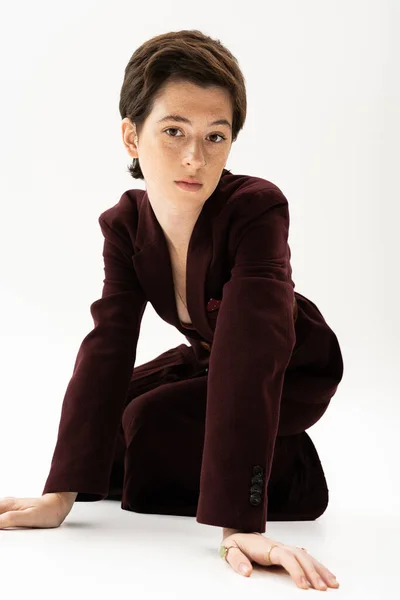 Young model with short brunette hair posing in brown pantsuit and looking at camera on white background — Stock Photo