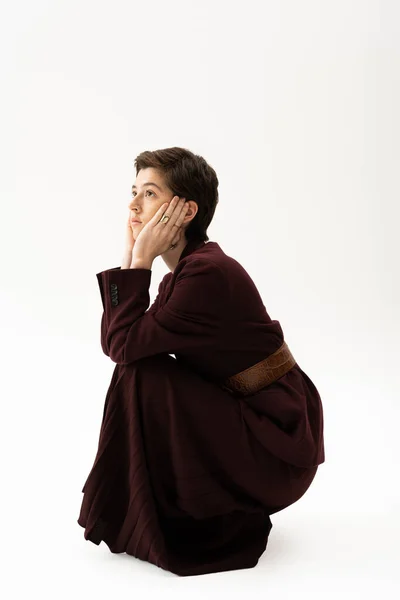 Mujer de ensueño en traje marrón cogida de la mano cerca de la cara y mirando hacia otro lado sobre fondo blanco - foto de stock