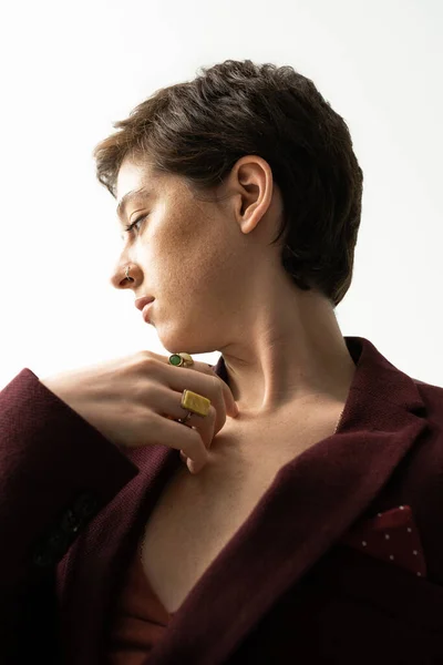 Sinnliche und verträumte Frau in Blazer und Fingerringen posiert mit brustnaher Hand auf grauem Hintergrund — Stockfoto