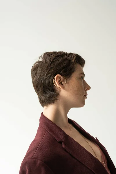 Profile of stylish brunette woman in cuff earring and blazer isolated on grey — Stock Photo