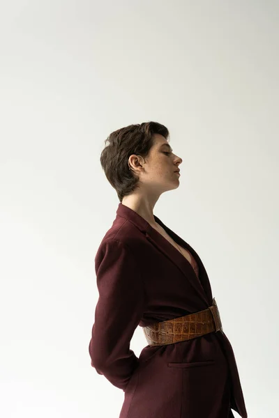 Vista lateral do modelo jovem morena em blazer e cinto de couro em fundo cinza — Fotografia de Stock