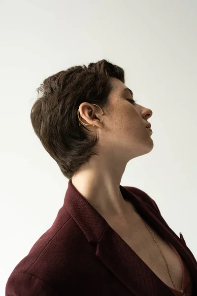 Seitenansicht der sinnlichen jungen Frau in Manschettenohrring und stylischem Blazer isoliert auf grau — Stockfoto