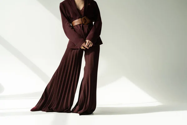 Visão parcial da mulher em calças largas e blazer com cinto de couro em fundo cinza com iluminação — Fotografia de Stock