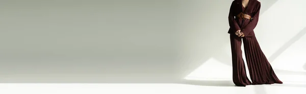 Обрезанный вид модели в брюках палаццо и пиджаке с кожаным поясом на сером фоне с освещением, баннер — стоковое фото