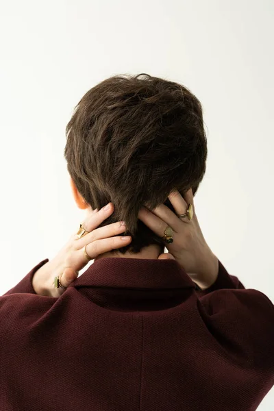 Back view of brunette short haired woman in finger rings posing with hands behind neck isolated on grey — Stock Photo