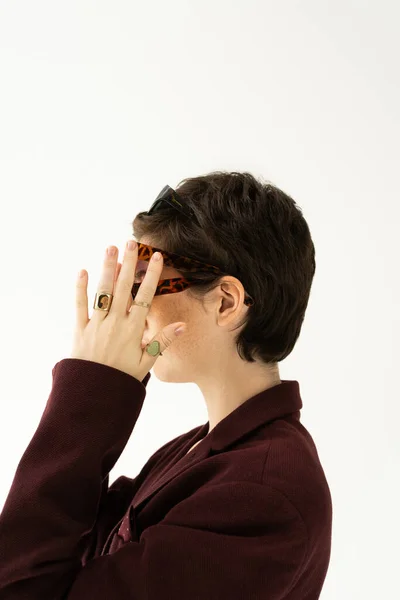 Вид сбоку брюнетки с короткими волосами в кольцах и нескольких солнцезащитных очках, изолированных на сером фоне — стоковое фото
