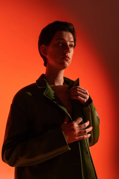 Mulher na moda em jaqueta de couro verde olhando para longe no fundo laranja sombreado — Fotografia de Stock
