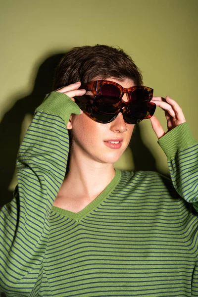 Junge Frau im trendigen gestreiften Pullover mit mehreren Sonnenbrillen auf grünem Hintergrund — Stockfoto
