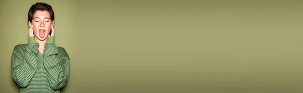 Élégante femme brune avec les yeux fermés collant la langue sur fond vert, bannière — Photo de stock
