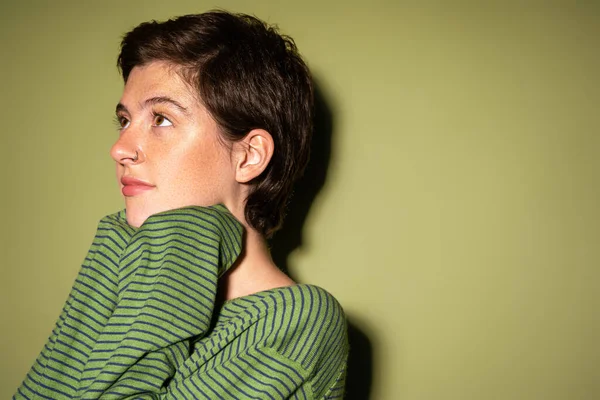 Junge und verträumte Frau im trendigen gestreiften Pullover auf grünem Hintergrund — Stockfoto