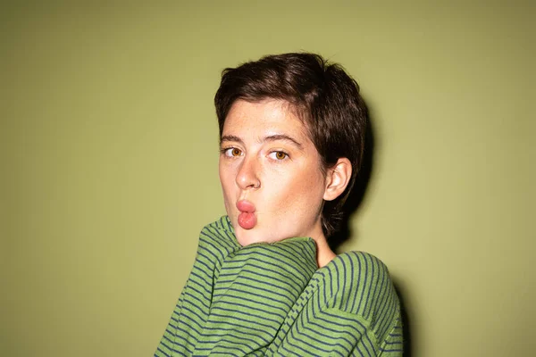Lustige Frau im gestreiften Pullover schmollende Lippen, während sie in die Kamera auf grünem Hintergrund schaut — Stockfoto