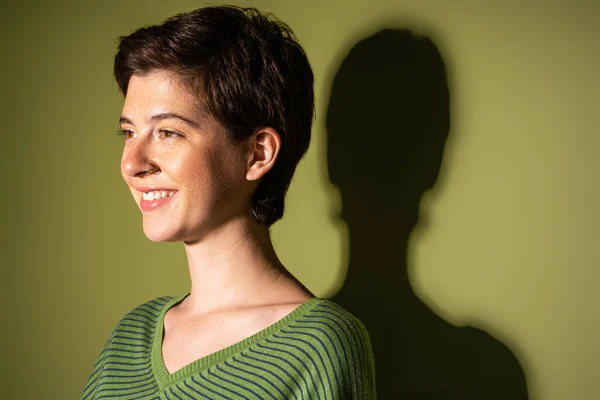 Porträt einer jungen und fröhlichen Frau im Frühlingspullover, die vor grünem Hintergrund mit Schatten wegschaut — Stockfoto