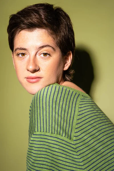 Porträt einer brünetten sommersprossigen Frau im Frühlingspullover, die in die Kamera auf grünem Hintergrund mit Schatten blickt — Stockfoto