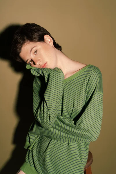Вдумчивая женщина в полосатом свитере смотрит в камеру на зеленом фоне с тенью — стоковое фото
