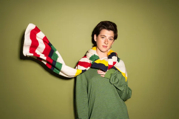 Молодая брюнетка в весеннем свитере и полосатый разноцветный шарф размахивая на ветру на зеленом фоне — стоковое фото
