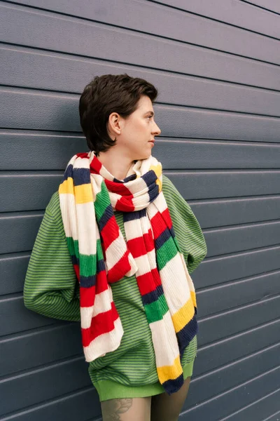 Брюнетка в смугастому шарфі дивиться далеко біля сірої стіни на міській вулиці — стокове фото