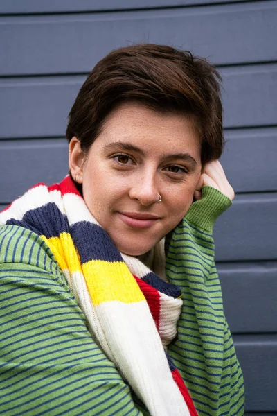 Portrait of carefree freckled woman in striped multicolored scarf looking at camera near grey wall on street — Stock Photo