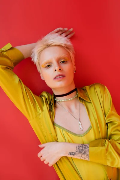 Портрет стильной альбиносы с яркой подводкой для глаз и татуировкой, смотрящей в камеру на кармине розового цвета — стоковое фото