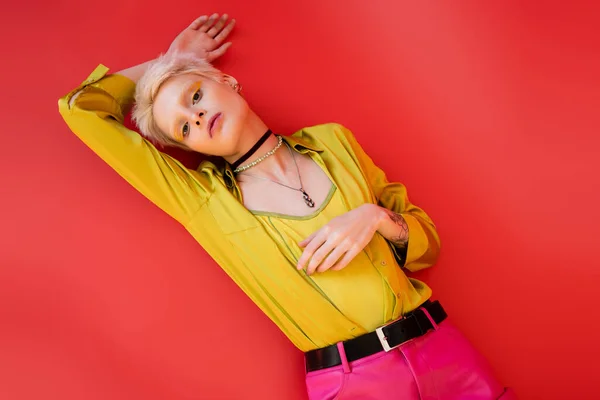 Vista dall'alto della donna albina alla moda con eyeliner luminoso e tatuaggio guardando la fotocamera su sfondo rosa carminio — Foto stock