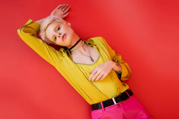 Top view of trendy albino woman with bright eyeliner and tattoo looking at camera on carmine pink background — Stock Photo