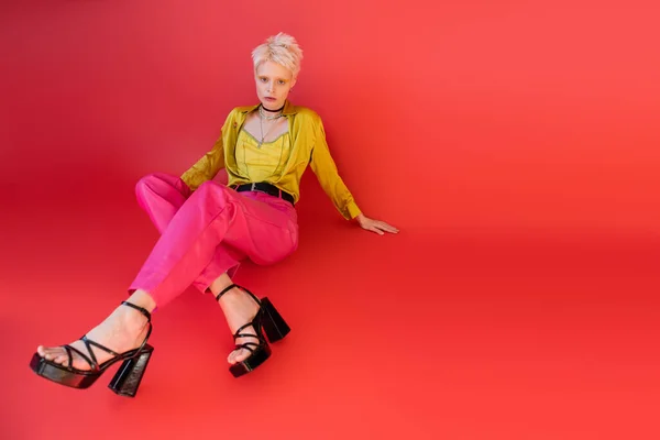 Полная длина блондинка модель в модной одежде и сандалии на каблуках позируя на кармине розовый фон — стоковое фото