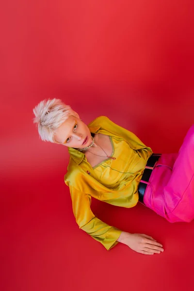 Overhead view of young albino model in trendy blouse and pants posing on carmine pink — Stock Photo