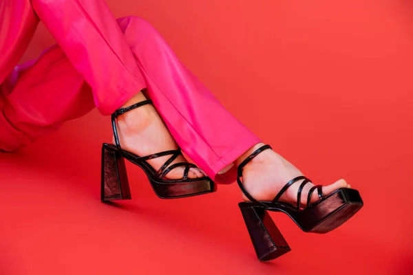 Cropped view of woman in trendy color pants and heeled sandals posing on carmine pink background — Stock Photo