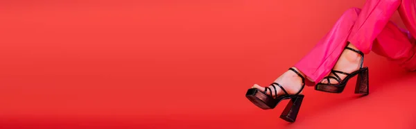 Vue partielle de la femme en pantalon de couleur à la mode et sandales à talons posant sur fond rose carmin, bannière — Photo de stock