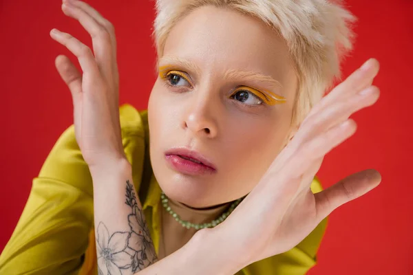 Mujer albina tatuada con delineador de ojos brillante mirando hacia otro lado mientras posa en rosa carmín - foto de stock