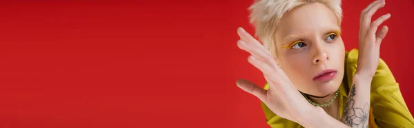 Donna albina tatuata con eyeliner giallo che distoglie lo sguardo mentre posa sul rosa carminio, banner — Foto stock