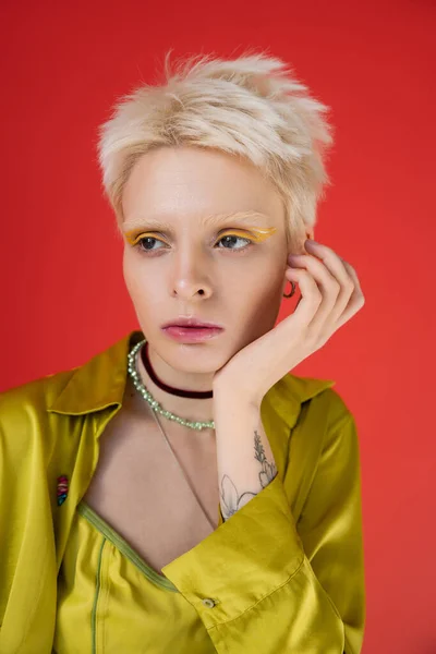 Porträt einer tätowierten und blonden Frau mit hellem Eyeliner, die auf karminrosa wegschaut — Stockfoto