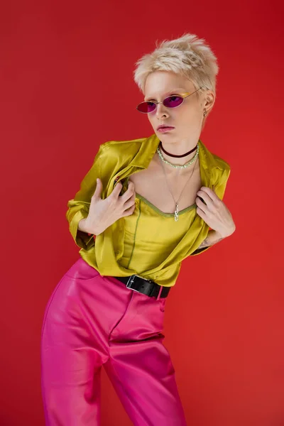 Modelo albino tatuado em roupa brilhante e óculos de sol na moda posando em rosa carmim — Fotografia de Stock
