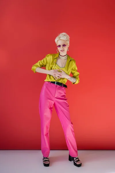 Glückliches Albino-Model in voller Länge mit tätowierter Hand posiert in stylischen Absatzsandalen auf karminrosa — Stockfoto