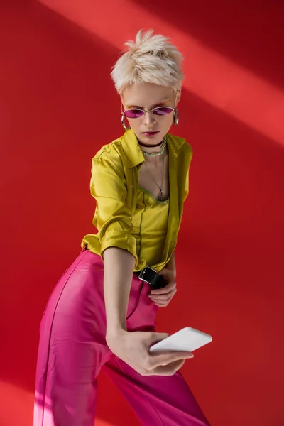 Альбиноса женщина в модных солнцезащитных очках делает селфи на смартфоне на кармине розовый — стоковое фото
