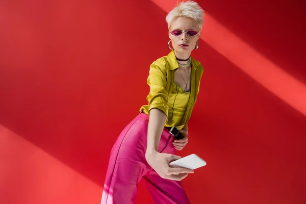 Женщина-альбинос в модных солнцезащитных очках делает селфи на смартфоне на розовом фоне — стоковое фото