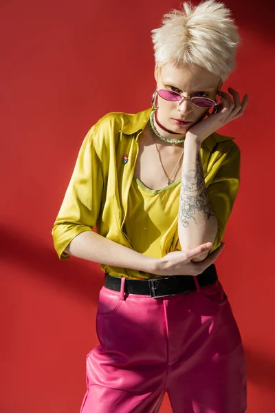 Sunlight on face of albino woman with tattoo posing in stylish sunglasses on carmine pink — Stock Photo